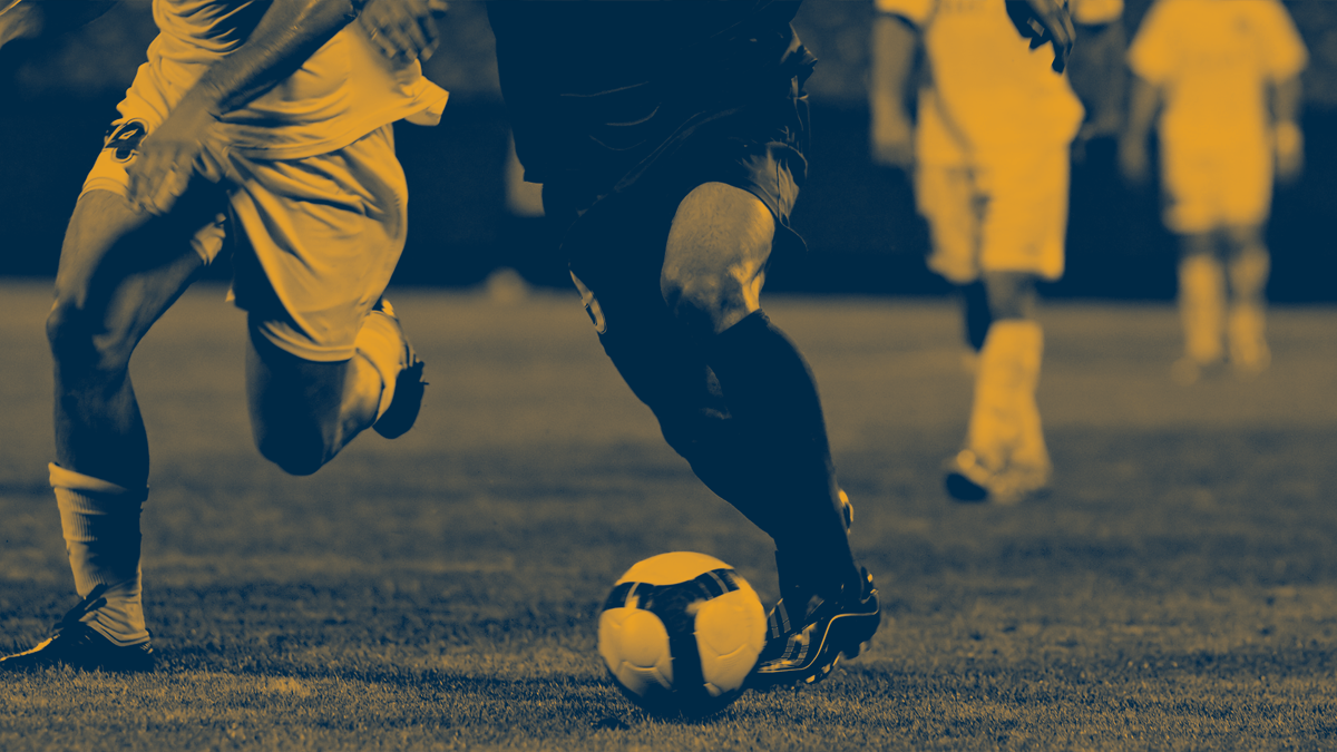 Närbild av två fotbollsspelare i duell om bollen under en match, med flera spelare i bakgrunden.
