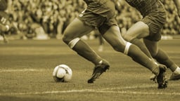 Två spelare tävlar om bollen i en fotbollsmatch.