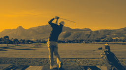 Golfspelare svingar klubban på en driving range med berg i bakgrunden under en solig dag.