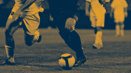 Närbild av två fotbollsspelare i duell om bollen under en match, med flera spelare i bakgrunden.